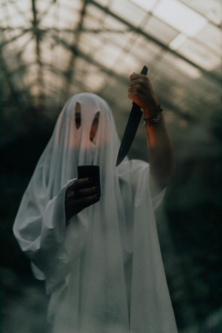 Creepy ghost costume holding a knife inside a dimly lit greenhouse, perfect for Halloween themes.